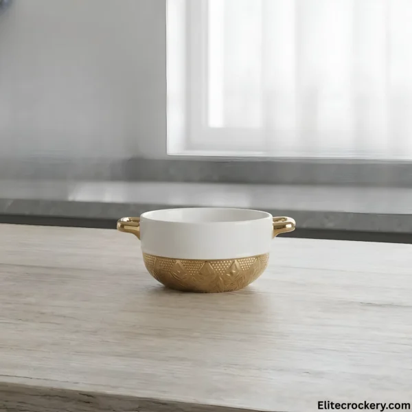 Ceramic soup bowl with gold handles on wooden table near window