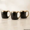 Set of three luxury black ceramic mugs with gold handles on marble counter